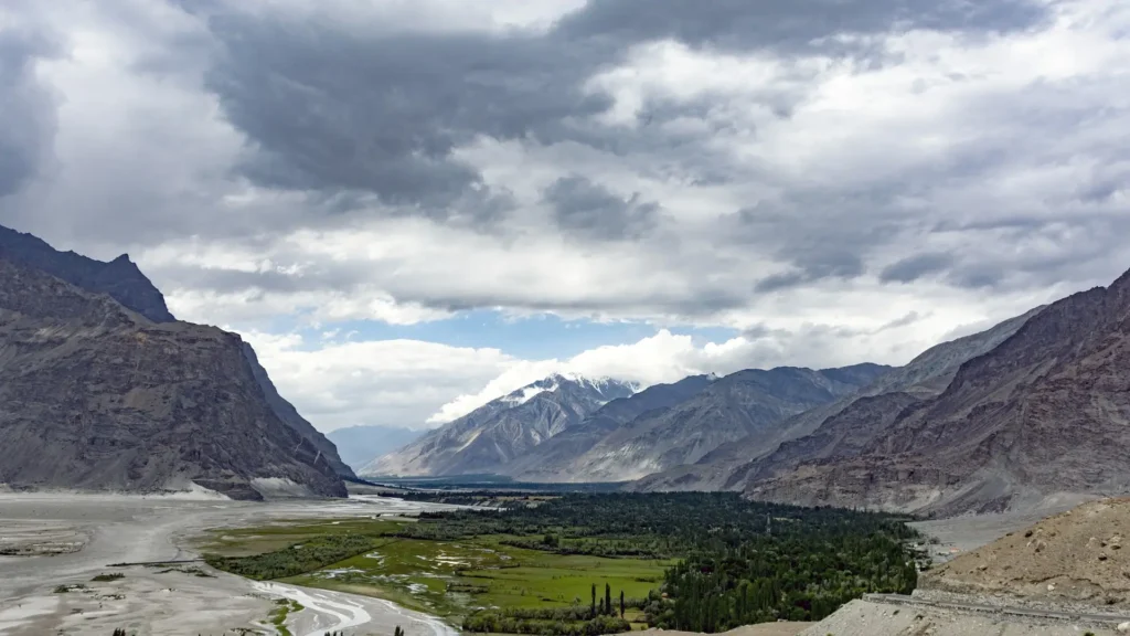 Lush green Shigar Valley oasis with a winding river surrounded by rugged Karakoram mountains under a dramatic cloudy sky in Gilgit-Baltistan Pakistan.