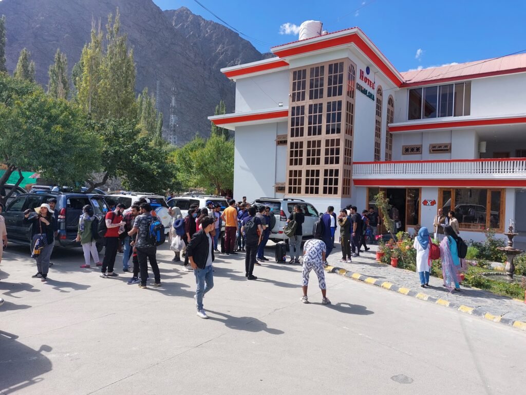 Tourists gathering outside Hotel Himalaya in Skardu, Gilgit-Baltistan with mountains and green trees in the background.