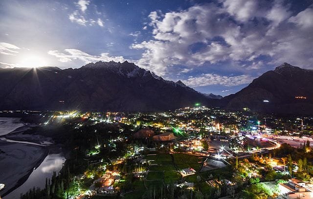 Panoramic night view of Skardu City illuminated by glowing lights under a bright moonlit sky in Baltistan, Pakistan.
