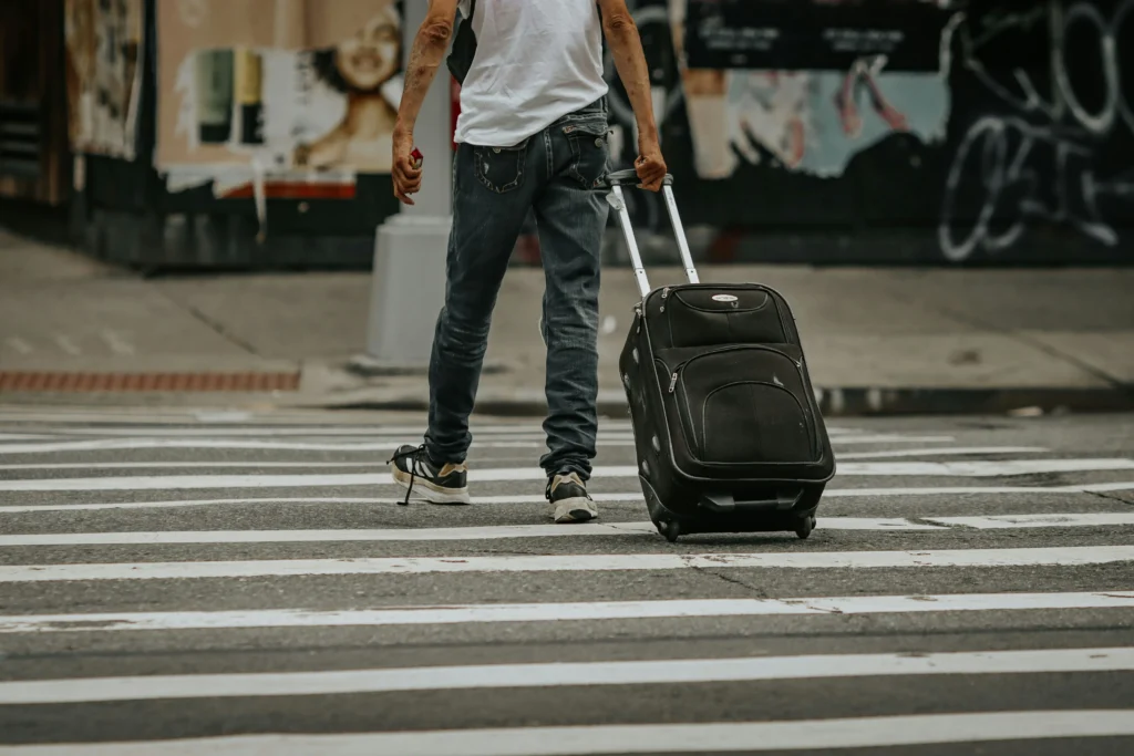 A traveler pulling a black rolling suitcase across a crosswalk while embarking on an adventure with Northern Discover travel agents.