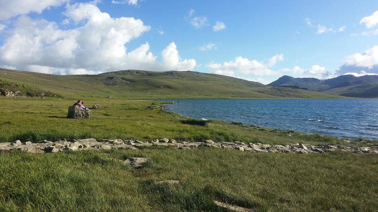 Sheosar Lake in Deosai National Park Pakistan with green rolling plains and blue waters under a cloudy sky.