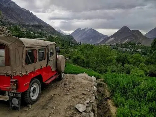 Jeep on a rugged mountain road overlooking the green valleys and mountains of Karimabad Hunza