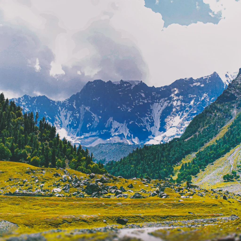 Gargo Meadows in Bagrot Valley, Pakistan, with rocky terrain in the foreground and majestic, snow-capped mountain peaks rising under a cloudy sky.