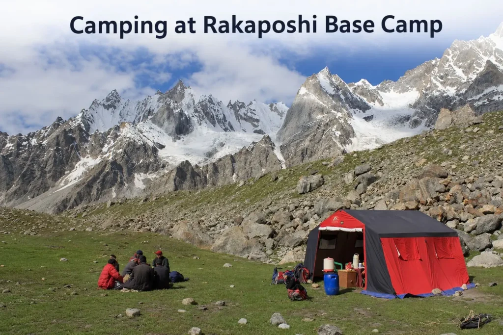 Rakaposhi Base Camp trekking camp with large red communal tent and group of trekkers sitting on a grassy slope, under massive snow-capped Karakoram peaks in Pakistan.