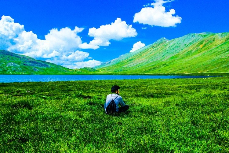 A person sitting in the vast green plains next to Sheosar Lake in Deosai National Park, a scenic highlight among places to visit in Astore Valley
