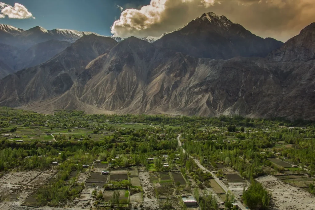 Scenic aerial view of green Gilgit Valley lush fields surrounded by rugged Karakoram mountain peaks under a dramatic cloudy sky
