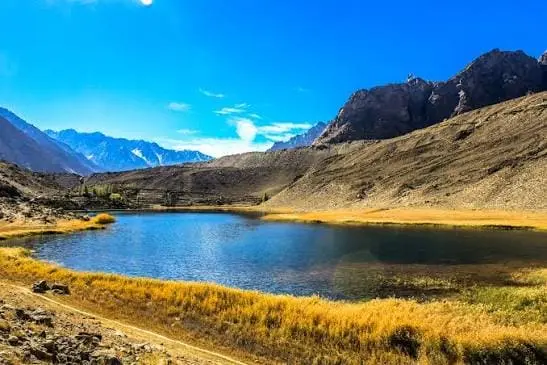 Scenic mountain lake surrounded by golden grass and rugged mountains in Northern Pakistan