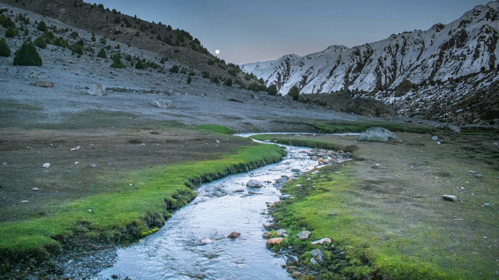 Stream flowing through Nanga Parbat Rupal Face Base Camp surrounded by snow-covered mountains